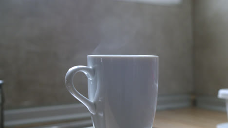 Beautiful-slow-motion-shot-of-a-white-mug-in-the-kitchen-billowing-smoke-or-steam-from-the-water-boiled-inside-to-prepare-tea-or-chamomile-tea-in-the-morning