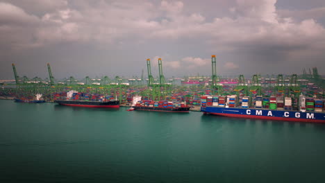 Container-ships-moored-to-dock-with-large-cranes-at-Port-of-Singapore,-aerial