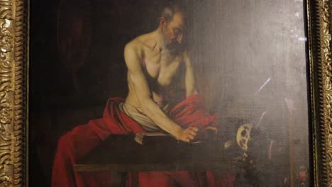 A-tilt-down-of-an-oil-painting-by-Caravaggio-depicting-Saint-Jerome-writing,-exhibited-in-the-Co-Cathedral-of-St