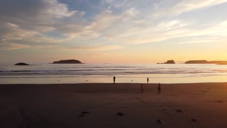 Drone-flying-over-silhouette-of-tourists-standing-on-beach-at-sunset