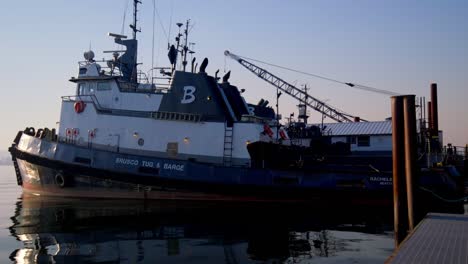 A-tied-up-tugboat-on-the-river,-anchored-securely-to-the-dock,-with-calm-waters-and-a-serene-backdrop,-highlighting-the-tranquility-and-charm-of-the-riverside-scene