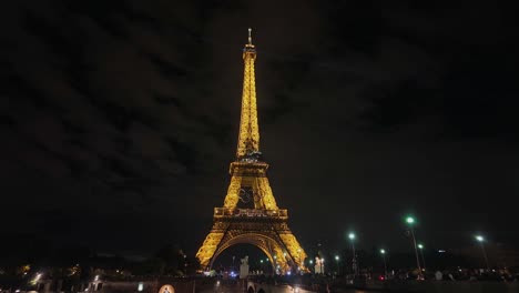 Tourists-on-the-Pont-d'Iéna-Bridge-with-the-illuminated-Eiffel-Tower-and-the-Olympic-Rings-logo-in-the-evening-background,-before-the-Games-2024-in-Paris,-France