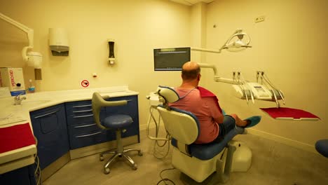 Male-patient-sitting-in-dental-chair-while-waiting-for-dentist-in-dental-clinic