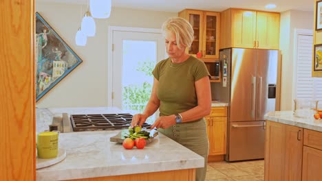 Side-angle-of-an-adult-woman-cutting-vegetables-and-fruit-on-a-wooden-board-in-a-modern-kitchen