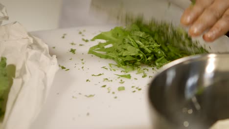 Close-up-of-hands-finely-chopping-fresh-herbs-on-a-white-cutting-board,-kitchen-setting