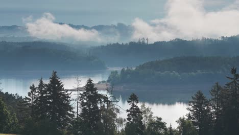 Exuberantes-Colinas-Verdes-Y-Bosques-Densos-Rodean-Un-Tranquilo-Lago-De-Montaña,-Ofreciendo-Una-Impresionante-Vista-Natural,-Mientras-La-Fina-Niebla-Se-Cierne-Sobre-El-Agua.