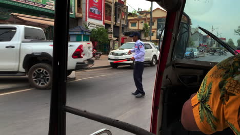 Cambodian-tuk-tuk-driver-in-Hawaiian-shirt-drives-by-mopeds,-cars,-and-traffic-cop,-moving-shot-passenger-pov