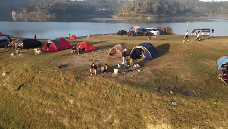 An-aerial-view-shows-several-people-camping-relaxing-and-cooking,-in-a-plain-area-near-the-Sermo-Reservoir,-Yogyakarta,-Indonesia