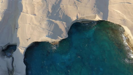 Aerial:-Rising-top-down-view-of-Sarakiniko-beach-in-Milos-island,-Cyclades,-Greece-during-sunrise