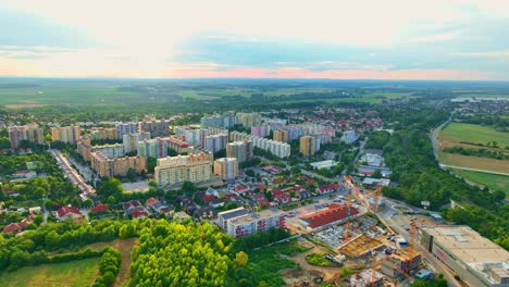 Aerial-drone-view-of-Devínska-Nová-Ves-with-residential-buildings,-green-spaces,-and-a-construction-site-under-a-cloudy-sky-during-sunset