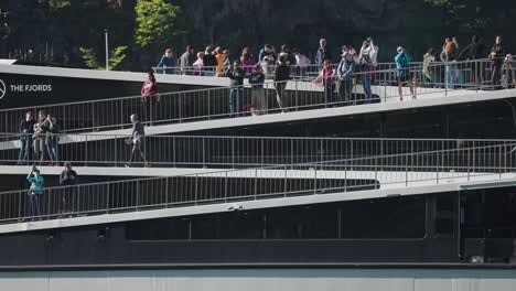 Un-Moderno-Ferry-Eléctrico-De-Pasajeros-Cruza-El-Fiordo-De-Naeroy,-Con-Numerosos-Pasajeros-Apiñados-En-La-Cubierta-Para-Disfrutar-De-La-Vista.