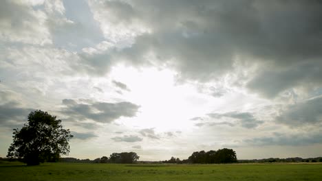 Sonnenbeschienene-Wolken-über-Einem-Grünen-Feld-Mit-Dynamischer-Schwenkbewegung,-Die-Eine-Ruhige-Ländliche-Landschaft-In-Der-Abenddämmerung-Einfangen