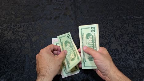 Close-up-shot-of-hands-sorting-US-currency-on-a-table-with-a-dark-background