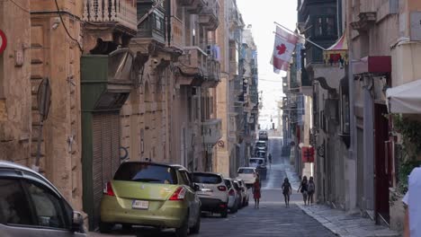 Una-Calle-Estrecha-Y-Vibrante-En-Malta-Llena-De-Edificios-Coloridos,-Con-Turistas-Y-Lugareños-Caminando.