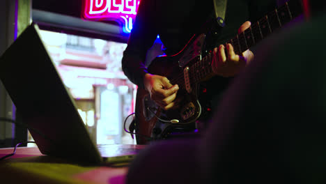 Hermosa-Toma-En-Cámara-Lenta-De-Un-DJ-Guitarrista-Con-Una-Computadora-Probando-El-Sonido-Para-Comenzar-Su-Espectáculo-En-Un-Bar-De-Discoteca-Con-Luces-De-Neón.