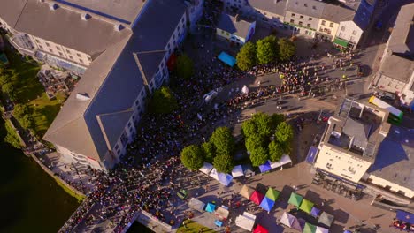 High-aerial-view-of-Spanish-Arch-in-Galway,-showcasing-the-end-of-the-Pegasus-Parade-during-the-Arts-Festival,-with-streets-bustling-with-crowds