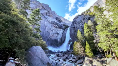 Majestuosa-Cascada-En-El-Parque-Nacional-De-Yosemite-Que-Cae-En-Cascada-Por-Un-Acantilado-De-Granito,-Rodeada-De-Frondosos-árboles-Verdes-Y-Grandes-Rocas.