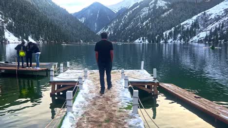 Man-walks-on-wooden-pier-in-a-big-almaty-lake