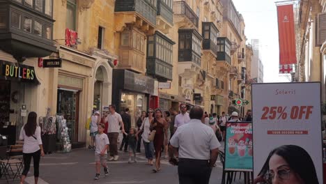 Una-Vista-Atractiva-De-Una-Calle-Estrecha-En-El-Centro-Urbano-De-Malta,-Que-Resalta-La-Combinación-De-Comercio-Moderno-Y-Diseño-Tradicional,-Llena-De-Actividad-Diaria.