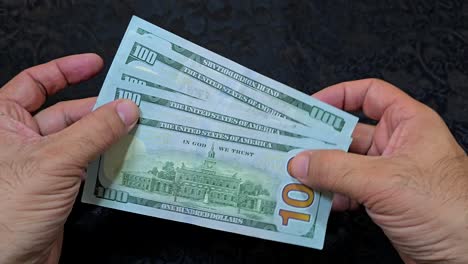 Hands-counting-US-dollar-bills-on-a-table,-dark-background,-close-up