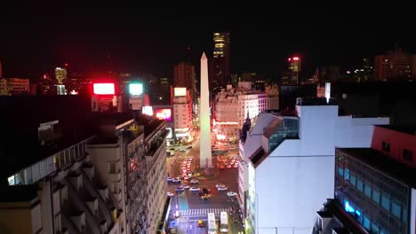 Aerial-night-view-going-up-over-Corrientes-Avenue-from-9-de-Julio-Avenue-and-the-obelisk,-the-city-lights-at-night-and-the-buildings-of-of-Buenos-Aires,-Argentina