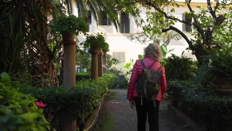 A-tourist-wearing-a-backpack-explores-the-lush-gardens-in-Palma,-Mallorca,-surrounded-by-greenery-and-historic-architecture