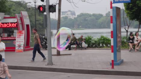 Bubbles-floating-on-the-street-full-of-people,-buggy-car-passing-by