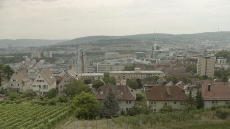 A-dense-urban-area-with-varied-architecture-and-green-hills-in-the-background,-cloudy-day,-aerial-view