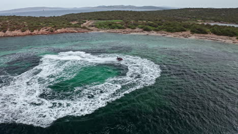 Turquoise-waves-forming-circular-patterns-near-a-rocky-shoreline,-aerial-view