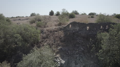 Abandoned-basalt-houses-and-a-jewish-village-in-the-area-of-Ein-Peak,-its-a-spring-in-the-south-of-the-golan-heights-and-a-remains-of-a-syrian-village,-kibbutz-afik-in-the-background