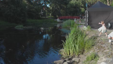 kid-playing-at-a-festival-and-throwing-pebbles-and-little-rocks-into-a-river-close-by-to-them-in-slow-motion