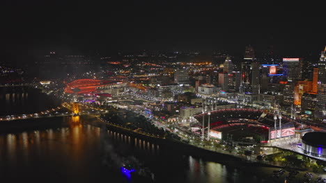 Cincinnati-Ohio-Aerial-v45-flyover-river-capturing-waterfront-ball-park,-vibrant-city-lights-and-spectacular-fireworks-over-a-bustling-night-downtown---Shot-with-Inspire-3-8k---September-2023