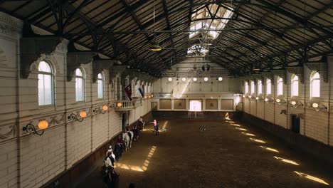 View-on-the-indoor-horse-riding-arena-at-Hollandsche-Manege-with-horses,-an-instructor,-and-children