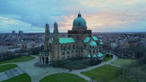 Aerial-drone-view-acending-the-basilica-of-the-sacred-heart-in-Brussels,-Belgium-on-a-beautiful-sunset-cloudy-sky