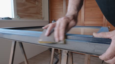 Older-adult-man-using-sandpaper-for-sanding-a-window-frame-for-painting