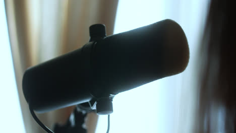 Beautiful-slow-motion-shot-of-a-famous-Shure-microphone-used-for-podcasting-in-a-recording-studio-in-the-morning-as-sunlight-streams-in-through-the-balcony