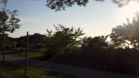 Promenade-by-sea-and-trees-at-sunset-by-Visby-at-Gotland,-Sweden,-POV-from-car