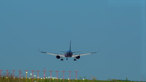 commercial-airplane-landing-on-a-runway-with-navigation-lights,-evening-sky-in-the-background---slow-motion