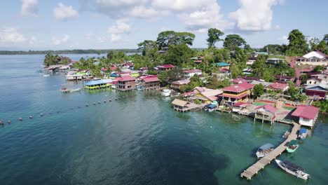 Vista-Aérea-Que-Muestra-Casas-Coloridas-A-Lo-Largo-De-La-Costa-De-La-Isla-Bastimentos,-Panamá,-En-El-Distrito-De-Bocas-Del-Toro-Con-Exuberante-Vegetación-Y-Aguas-Azules-Cristalinas.