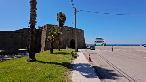 Historic-coastal-fortress-near-the-sea-with-a-ferry-docked-under-a-clear-blue-sky