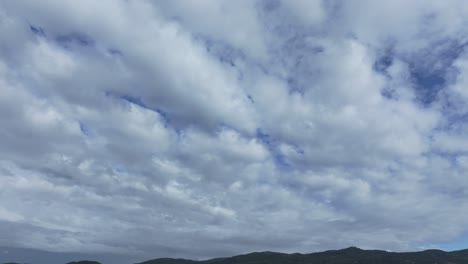 Vuelo-Con-Drone-Visualizando-Una-Hilera-De-Montañas-Al-Fondo-Del-Rodaje-Y-Como-Plano-Principal-Un-Cielo-Completamente-Cubierto-De-Nubes,-Se-Ven-Pinceladas-Azules-Del-Cielo-Entre-Nubes