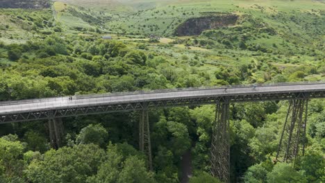 Two-cyclists-crossing-an-old-viaduct-with-a-scenic-backdrop-of-lush-green-hills-and-valleys