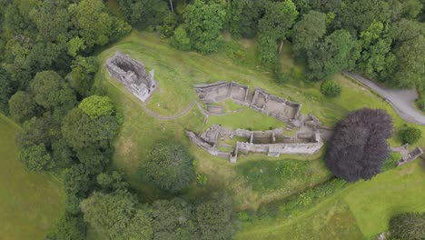 Aerial-fly-over-capturing-Okehampton-Castle-amidst-dense-greenery-in-Devon,-UK