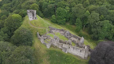 Drone-fly-up-showcasing-Okehampton-Castle-and-surrounding-woodland-in-Devon,-UK