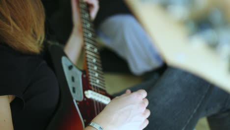 Beautiful-slow-motion-shot-of-a-young-blonde-woman-playing-a-vintage-Fender-Jaguar-electric-guitar-with-her-fingers-inside-her-room