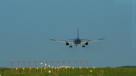 A-commercial-airplane-landing-on-a-runway-with-navigation-lights,-green-field-in-the-background