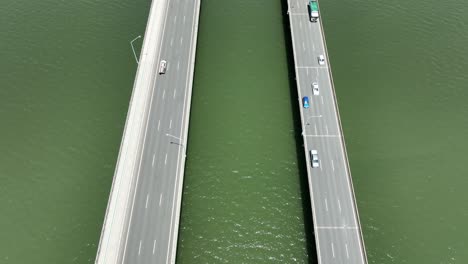 Drone-establishing-shot-of-Ted-Smout-Memorial-Bridge,-camera-flying-in-between-both-bridge-lanes,-descending-and-panning-up-revealing-the-greater-bridge-structure-and-Brisbane-in-background