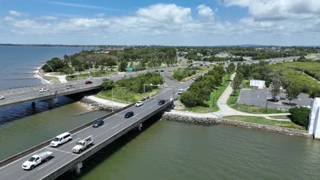 Drone-establishing-orbiting-of-Ted-Smout-Memorial-Bridge,-camera-flying-pull-away-and-ascending-over-water-Moreton-Bay-with-Brisbane-City-in-background