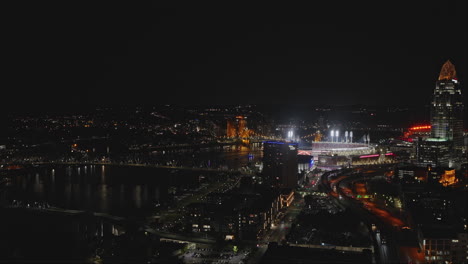 Cincinnati-Ohio-Aerial-v39-drone-flyover-the-freeway-capturing-riverside-arena,-game-playing-at-the-ball-park,-waterfront-downtown-cityscape-at-night---Shot-with-Inspire-3-8k---September-2023