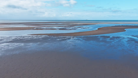 Aerial-shot,-Track-Forward,-Ripples-on-the-ocean-water-of-the-shallow-tide-pools-of-Forest-Beach-with-blue-sky-reflection,-Far-North-Queensland,-Australia